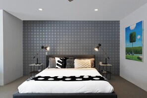 Ein modernes Schlafzimmer mit einer Wand mit Muster, einem Bett mit schwarz-weißem Punkte-Bettbezug, zwei Nachttischen mit Lampen und einem Bild an der Wand.