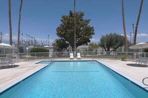 Ein rechteckiger Pool mit glasklarer, blauer Wasseroberfläche, umgeben von einem weißen Zaun, mit Palmen im Hintergrund.