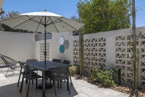 Eine Terrasse im Freien mit Tisch und Stühlen, einer Zierwand und einem Kaktus.