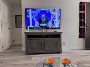 Ein Zimmer mit einem an einer Holzkabine montierten Fernseher, einem Glastisch mit zwei Schalen und einem gemusterten Vorhang.