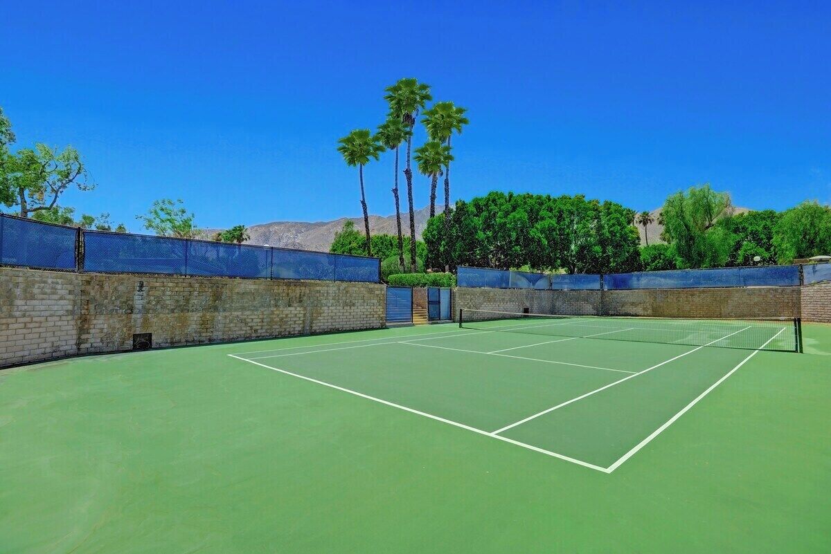 A tennis court with a net, surrounded by brick walls and palm trees.