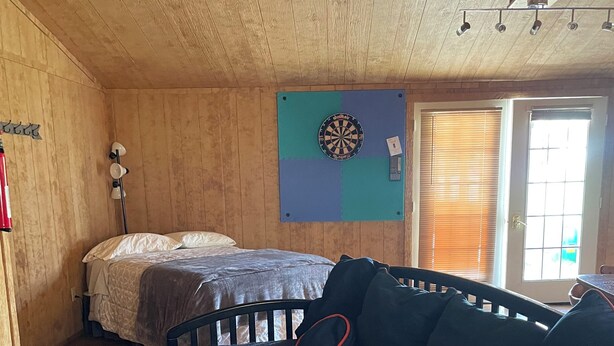 Ein Zimmer mit einem Bett, einem Babybett, einer Dartscheibe und einem Fenster mit Jalousien.