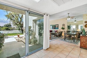 Ein geräumiger Wohnbereich mit einer Schiebetür zu einer Terrasse, ein Essbereich mit Tisch und Stühlen sowie ein Deckenventilator.