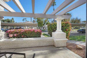 A covered outdoor area with a white pergola, a planter with pink flowers, and a stone column. - Mesquite Modern Dream (Palm Springs)