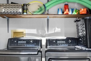 A laundry area with two washing machines, a shelf with various items, and a basket. - Mesquite Modern Dream (Palm Springs)