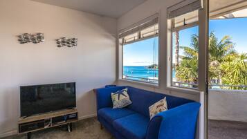 Ein Wohnzimmer mit einem Flachbildfernseher, einem blauen Sofa und Meerblick durch große Fenster.