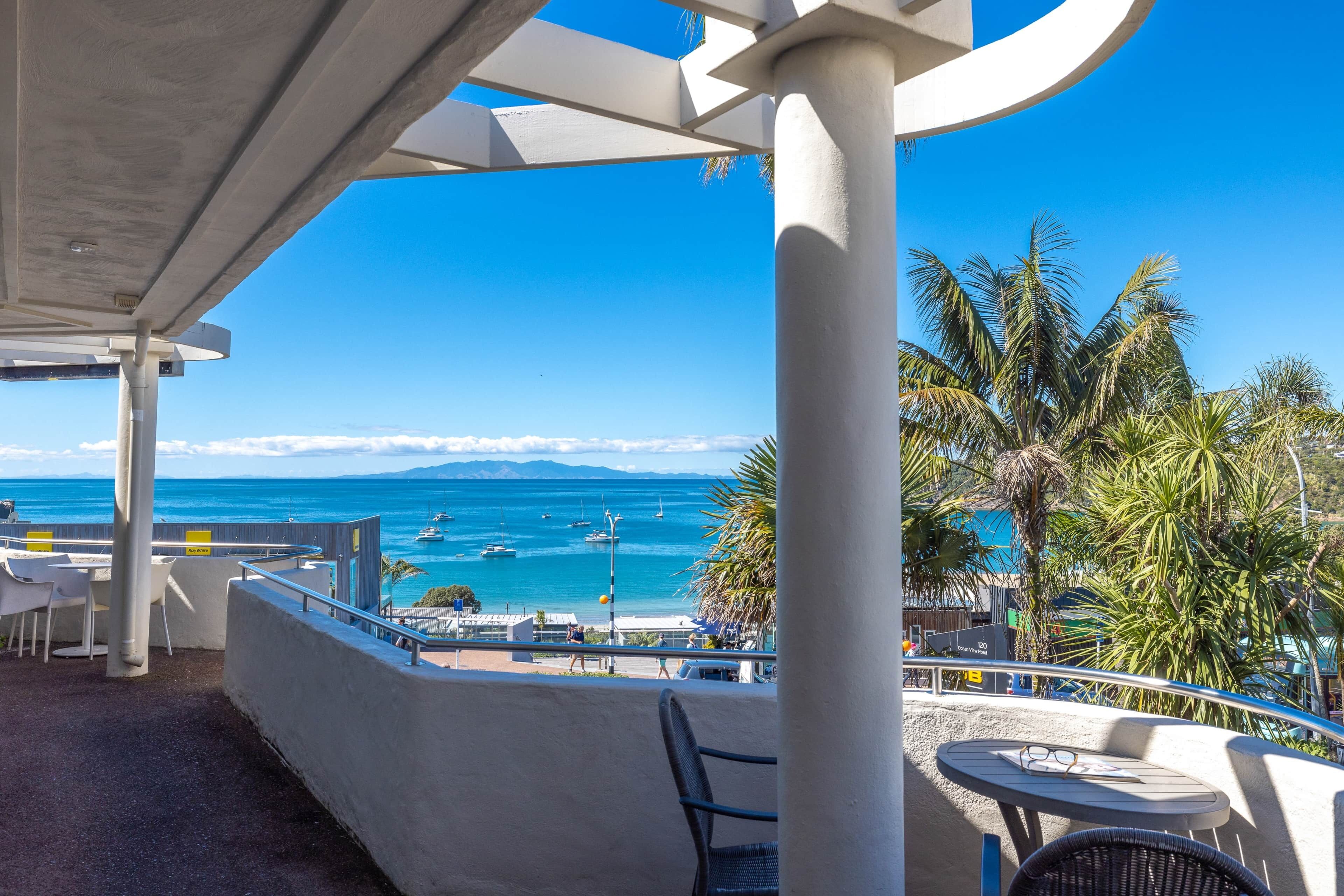 Eine Seeterrasse mit Blick auf das Meer und Boote, ausgestattet mit Sitzgelegenheiten im Freien und einer Palme.