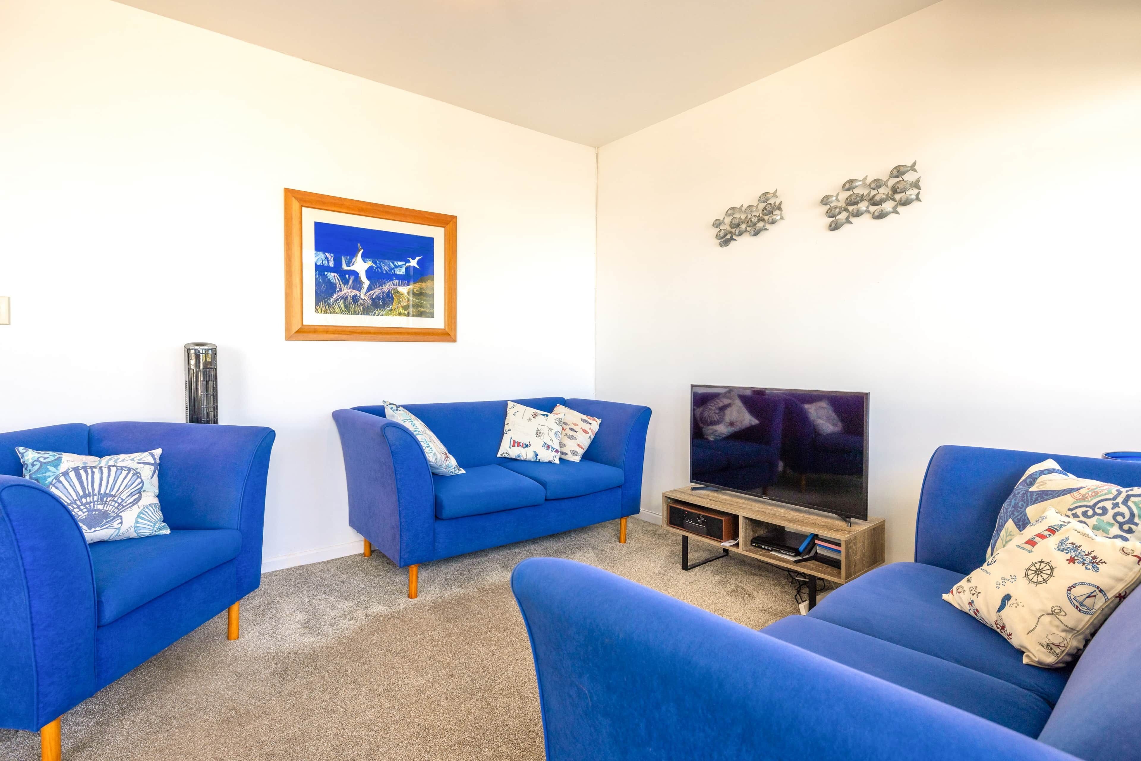 Ein Wohnzimmer mit blauem Sofagarnitur, einem Flachbildfernseher und einem gerahmten Bild an der Wand.