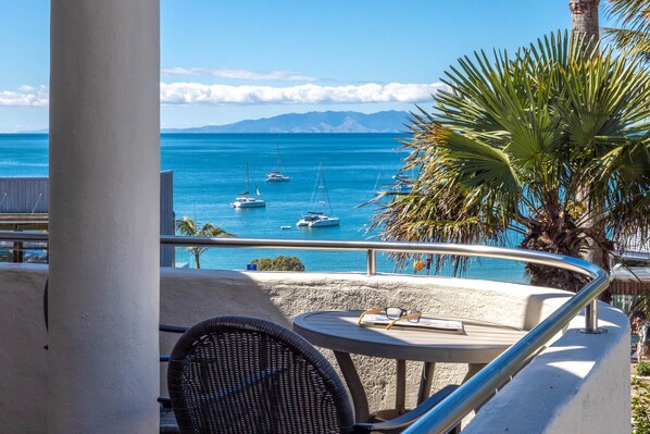 A balcony with a view of the sea, a chair, and a table with a book and glasses.