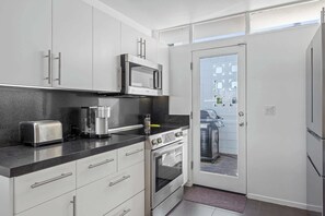 Eine moderne Küche mit weißen Schränken, einer eingebauten Mikrowelle, einer Kaffeemaschine, einem Toaster und einem Herd.
