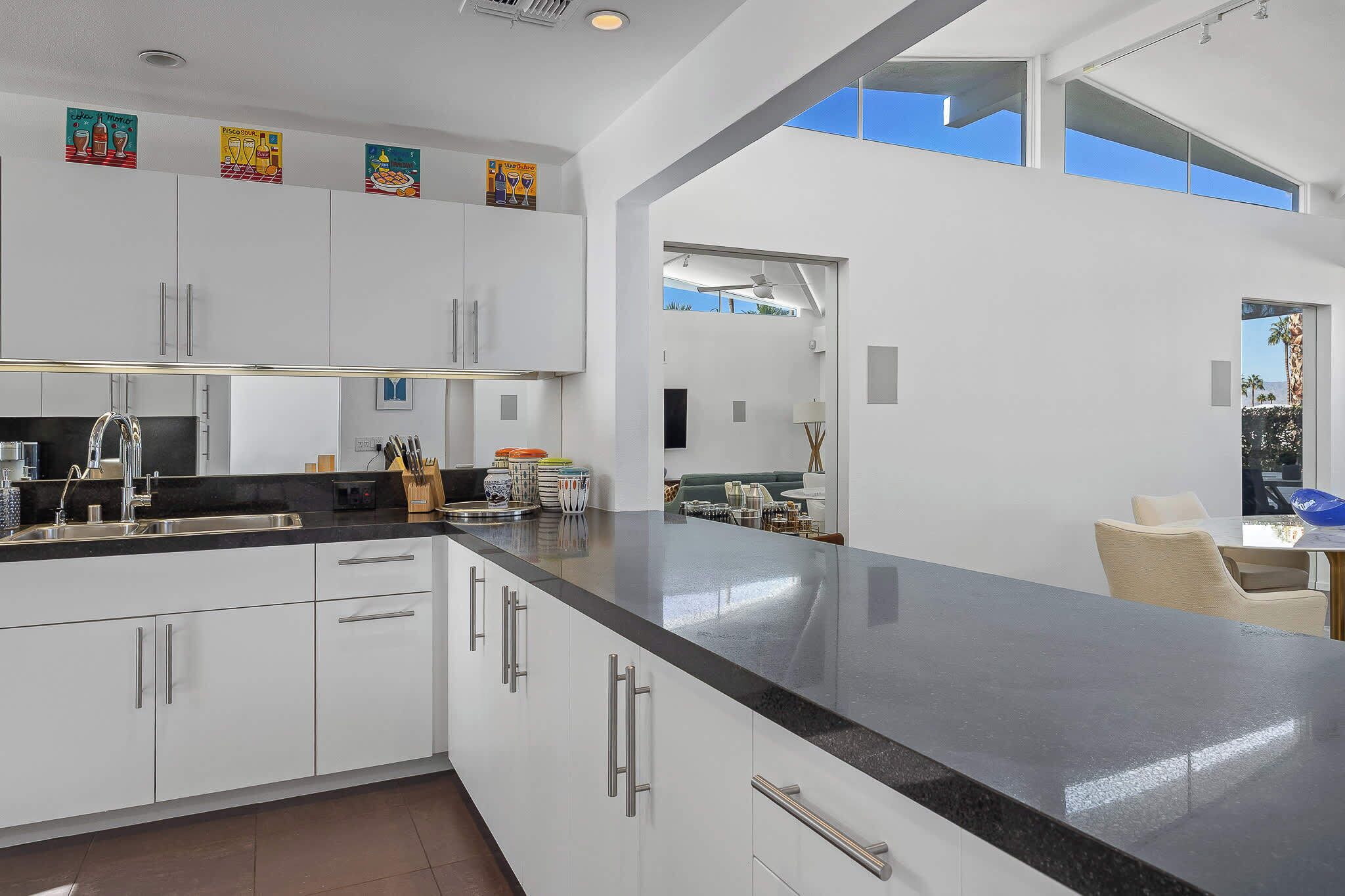 A modern kitchen with white cabinetry, a black countertop, and a view of the outdoors.