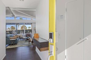 Ein modernes Wohnzimmer mit einer Couch, einem Couchtisch und Sesseln, ein Essbereich mit Tisch und Stühlen sowie ein großes Fenster mit Blick auf Palmen.
