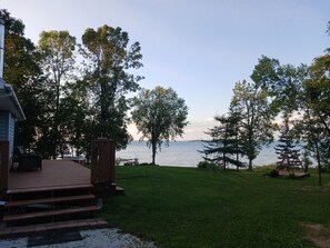 A deck with steps leading to a grassy area overlooking a body of water, surrounded by trees.