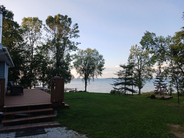 A deck with steps leading to a grassy area overlooking a body of water, surrounded by trees.