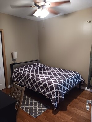 A bedroom with a bed, a ceiling fan, a nightstand, a lamp, a chair, and a rug.