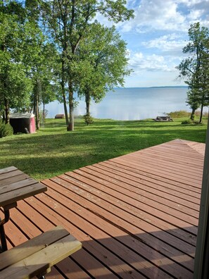 A wooden deck with a picnic table, surrounded by trees and overlooking a calm lake.