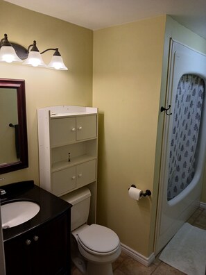 A bathroom with a toilet, sink, vanity, and a shower with a curtain.