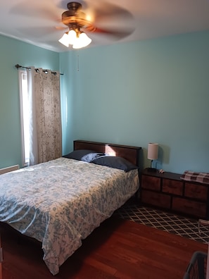 A bedroom with a bed, a nightstand, a lamp, a ceiling fan, and a window with curtains.