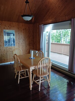 A wooden-paneled room with a dining table and chairs, a hanging light fixture, and a window with curtains.