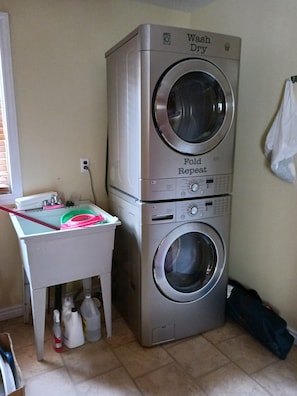 A stacked washer and dryer unit with a small table and cleaning supplies nearby.