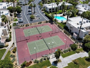 A tennis court with a pool in the background. - PS Golf and Tennis Stay (Palm Springs)
