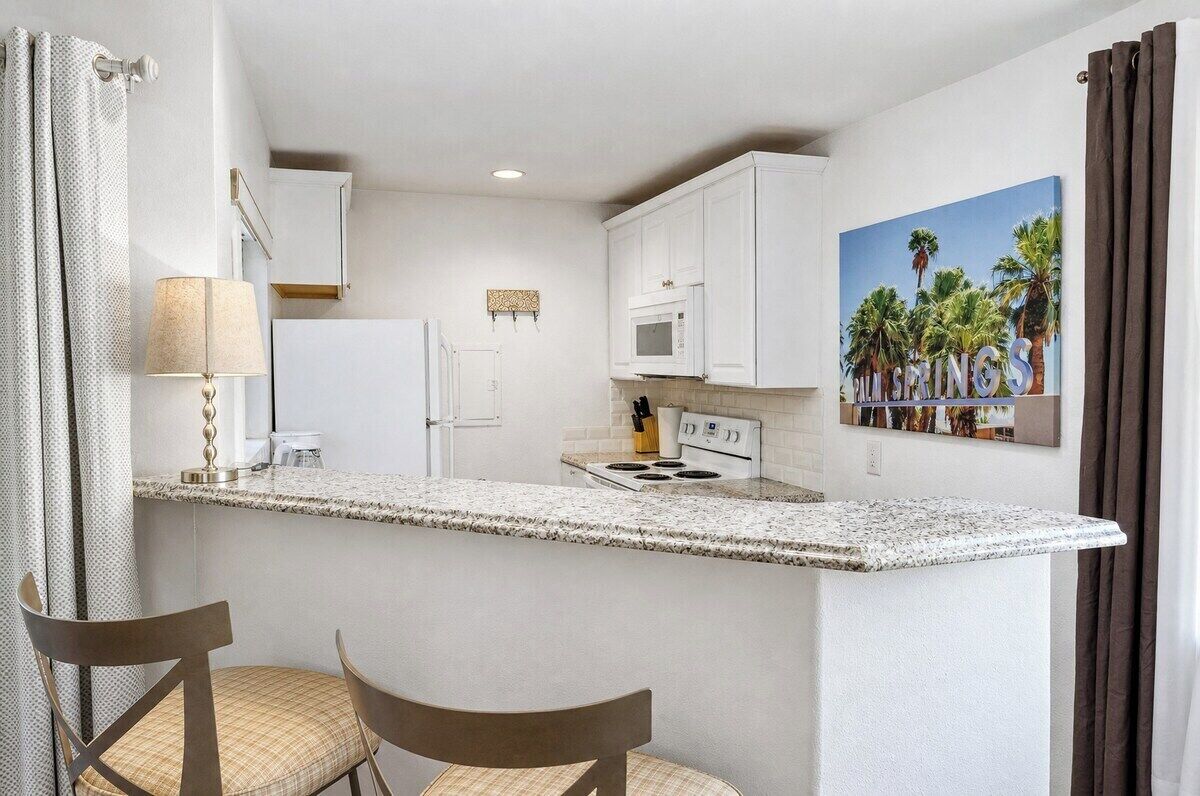 A compact kitchen with white cabinets, a microwave, a stove, and a small island with chairs.