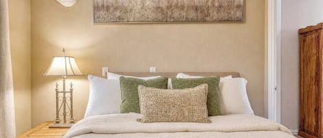 Un dormitorio con cama, una mesita de noche con lámpara, un cuadro en la pared y un armario de madera.