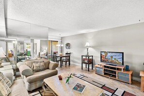 A modern living room with a sofa, coffee table, TV, and a dining area with chairs and a table. - PS Golf & Tennis Club Condo (Palm Springs)