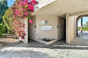 Una entrada d'edifici amb façana de formigó, un senyal de perill i una petita jardineria.