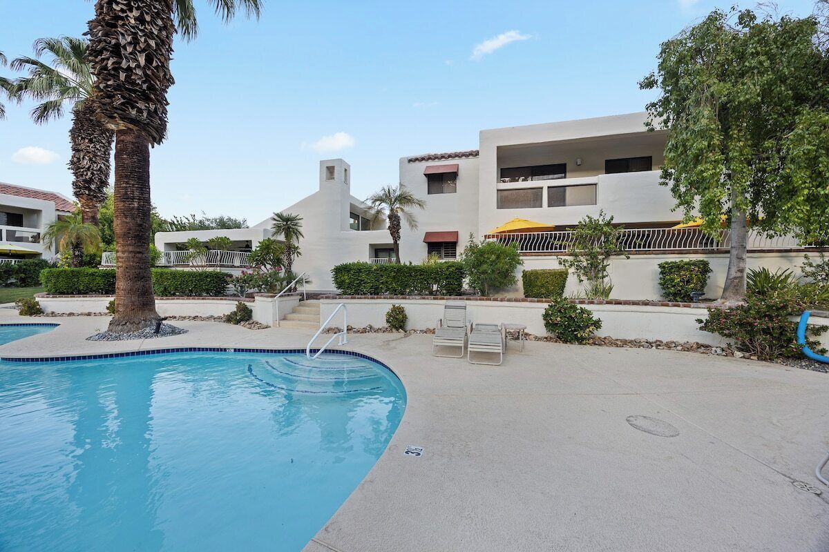 Une piscine bordée d’un palmier, un immeuble doté de balcons et un ciel dégagé.