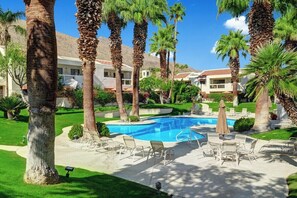 Zona de piscina con sillones de descanso y palmeras.
