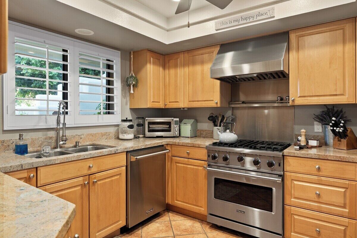 A kitchen with wooden cabinets, a stainless steel range, a dishwasher, and a window with blinds.