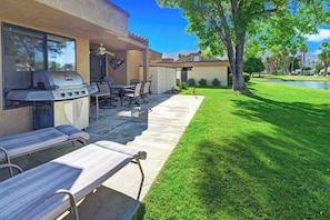 An outdoor patio with a grill, seating, and a view of a well-maintained lawn and trees. - Cathedral Canyon CC Oasis (Palm Springs)