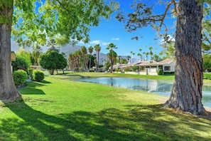 A well-maintained lawn with a small pond, surrounded by trees and a building with a tiled roof. - Cathedral Canyon CC Oasis (Palm Springs)