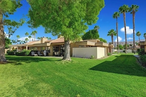 A residential property with a well-maintained lawn, a large tree in the foreground, and multiple palm trees in the background. - Cathedral Canyon CC Oasis (Palm Springs)