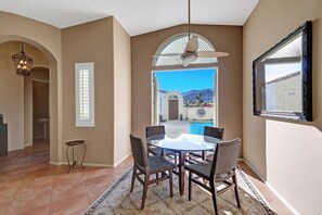 A dining area with a round table and chairs, a ceiling fan, and a view of a pool and mountains. - Hidden Jewel at Rio Del Sol (Cathedral City)