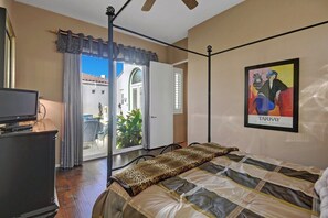 Une chambre à coucher avec un lit, une télévision, une porte donnant sur un balcon et un tableau accroché au mur.