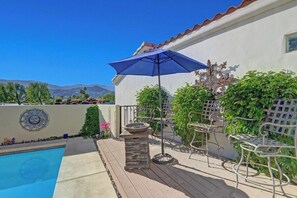 A poolside area with a patio, metal chairs, a blue umbrella, and a decorative wall. - Hidden Jewel at Rio Del Sol (Cathedral City)