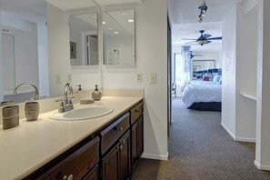 A hotel bathroom with a double sink, a large mirror, and a view into the bedroom. - Ramon Estados Treehouse (Palm Springs)