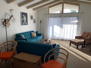 A living room with a blue sofa, a wooden chair, a wicker table, and a floor lamp. - Ramon Estados Treehouse (Palm Springs)