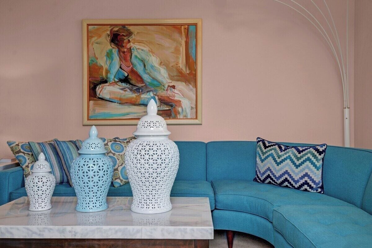 A room with a blue sofa, a white table with decorative vases, and a painting on the wall.