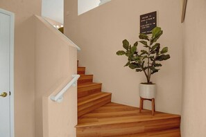 Eine Treppe mit Holzstufen und einem weißen Geländer, die zu einer Zwischenebene mit einem Blumentopf und einem Willkommensschild führt.