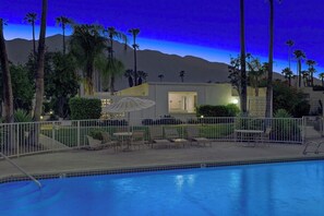 A swimming pool area with lounge chairs and a building with a door and windows. - Garden Villas Paradise (Palm Springs)