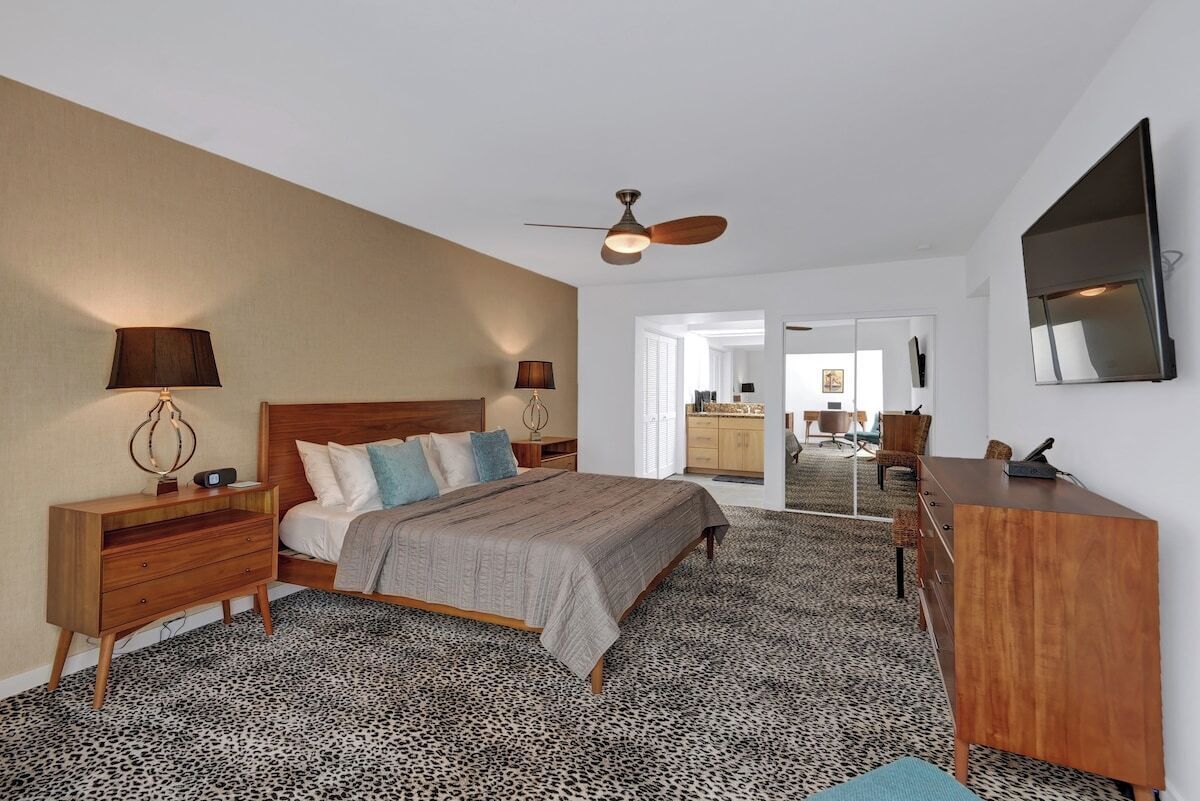 A bedroom with a bed, nightstands, a desk, a ceiling fan, and a large mirror.