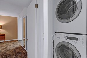 A laundry room with two stacked washing machines, a wooden dresser, and a leopard print carpet. - Garden Villas Paradise (Palm Springs)