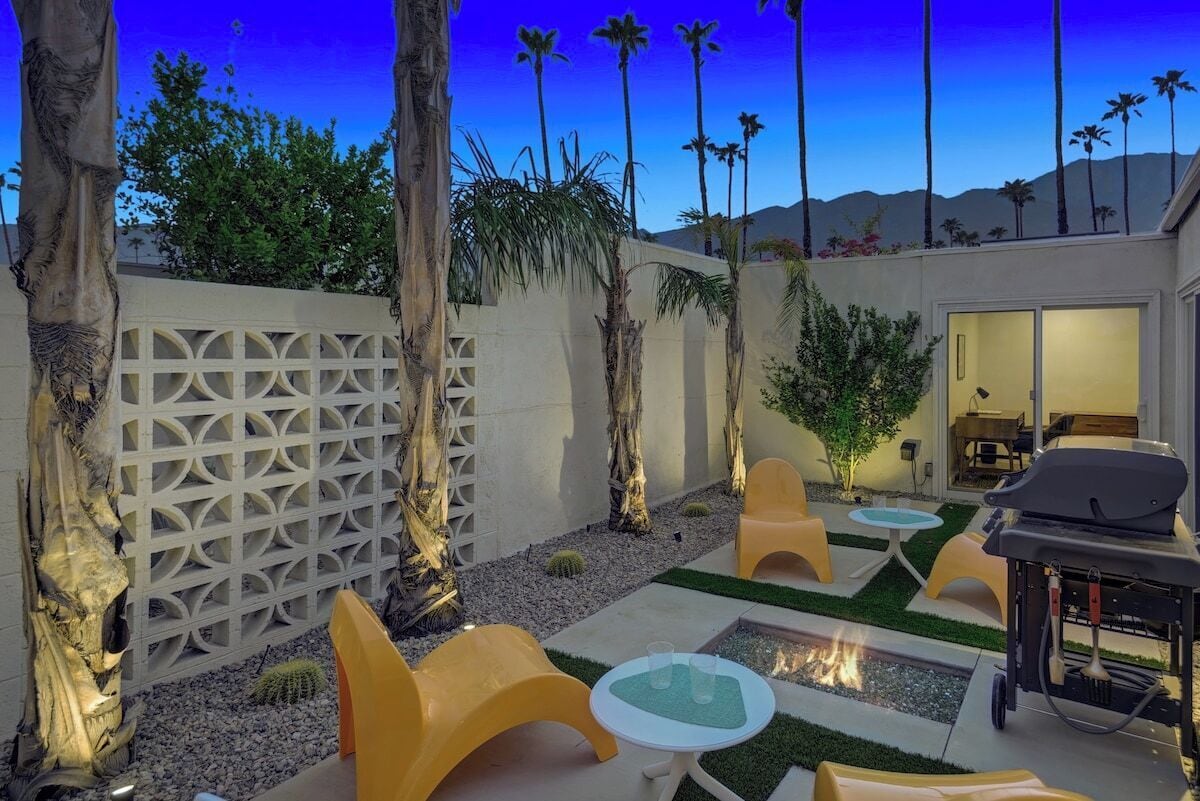 An outdoor patio area with seating, a grill, and a view of palm trees and mountains.
