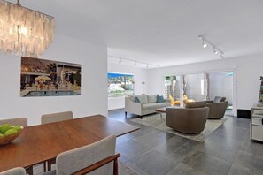 A modern living room with a dining area, a large chandelier, and a view of the outdoors. - Garden Villas Paradise (Palm Springs)