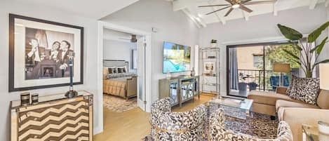 A spacious living area with a modern ceiling fan, a dining table with patterned chairs, a sofa, and a television.