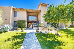 A two-story building with a covered outdoor area, a concrete pathway, and various landscaping including a tree and a cactus. - The Ricardo on Ramon (Palm Springs)
