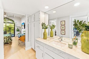 A modern bathroom with a large mirror, a sink, and two green vases. - The Ricardo on Ramon (Palm Springs)